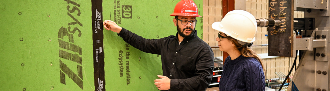 two people wearing hard hats standing in front of a green board